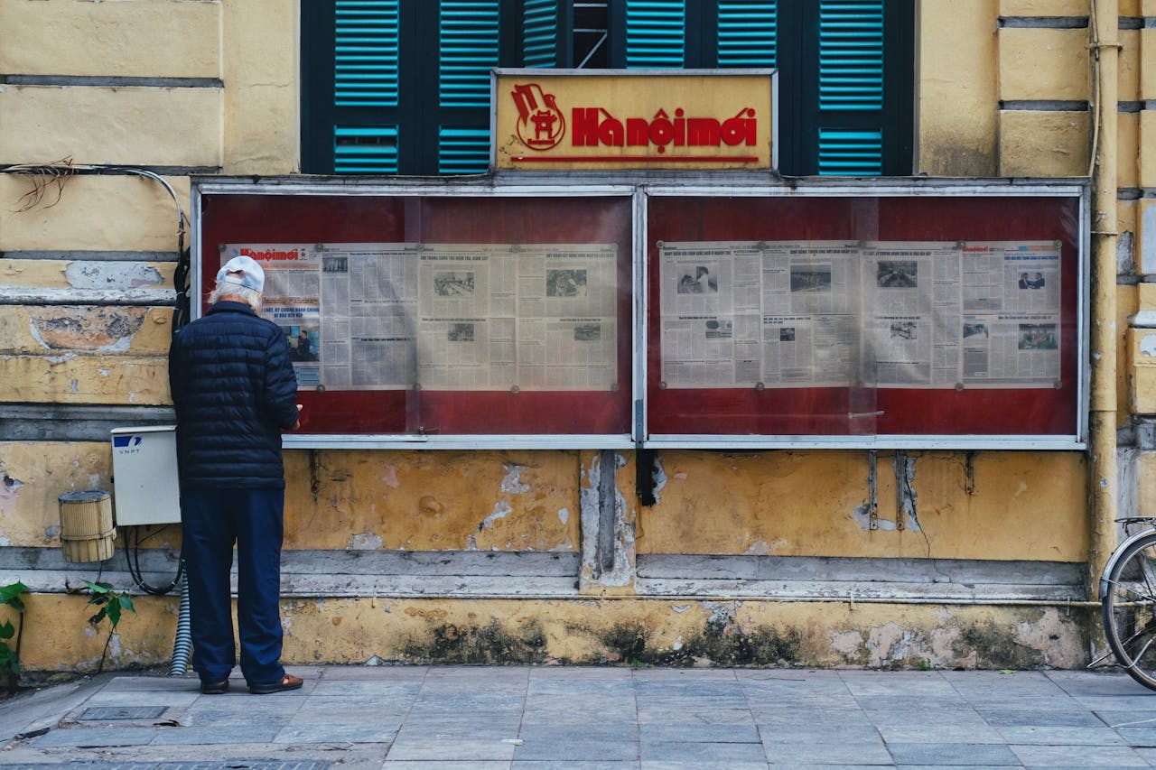 services-img An elderly man stands reading newspapers displayed in a glass case on a street in Hanoi, Vietnam.
