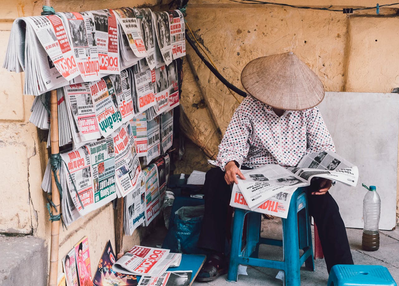 about-01 A street vendor in Hanoi reads newspapers, showcasing daily life in Vietnam.